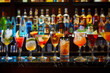 A row of glasses with various drinks on a bar counter