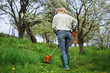 © encierro - Woman is cutting grass by weed trimmer in garden. Mowing lawn in orchard. Spring gardening