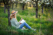 Woman is writing diary and resting in blossoming orchard. Mindfulness and reconnect the moment in spring nature