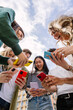 © Xavier Lorenzo - Vertical photo of young adult friends using mobile phone together outside. Gen Z people generation having fun watching social media content on cellphone app network.