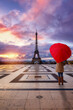 A woman with a heart shaped umbrella watches a romantic sunrise behind the Eiffel Tower of Paris, France