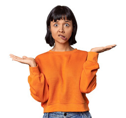 Poster - Young Hispanic woman with short black hair in studio confused and doubtful shrugging shoulders to hold a copy space.