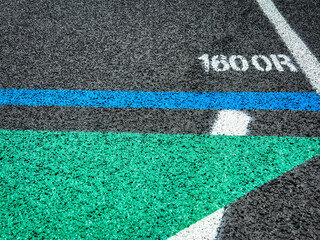 Track and Field Running Lanes. Overhead view of a rubber black running surface with white lane lines. Focus on the 1600 meter staggered start line. Blue start line and green arrow.