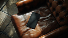 A Black Cell Phone Is Sitting On A Brown Leather Couch. The Couch Is In A Room With A Tan Floor