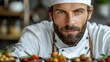   A bearded man in a chef's hat stands before bowls of fruit and vegetables