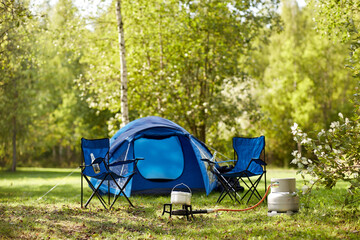 food cooking, tourism and travel concept - close up of camping pot on tourist gas burner, blue tent 