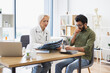 © sofiko14 - Mindful gray-haired female in lab coat holding MRI scan while brunette guy sitting next to her at desk in hospital. Family doctor examining diagnostic test results while developing treatment plan.