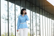 Successful elegant businesswoman entrepreneur or CEO in blue shirt and white pants smiles and talks on smartphone with partners or clients while walks by the office building outdoor. Business concept