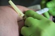 Hände von Ärztin mit grünen medizinischen Gummihandschuhen halten Spritze in Arm von Patientin bei Blutabnahme in Arztpraxis
