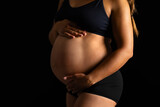 Fototapeta Sawanna - Pregnant Woman Embracing Her Belly in Dark Backdrop