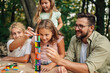 © Zamrznuti tonovi - Playful fun family playing board game at picnic table in nature.