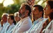 A group of doctors and nurses sitting in a row, listening to a presentation at an outdoor event. Soft sunlight
