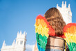 Trans young girl with rainbow wings on Madrid pride parade with city hall and blue sky background