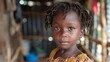 children of cte divoire, A young girl with braided hair and traditional clothing looks calmly at the camera in a rustic setting. 