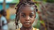 children of haiti, Portrait of a young girl with braided hair looking at the camera with a thoughtful expression in a blurred outdoor setting. 