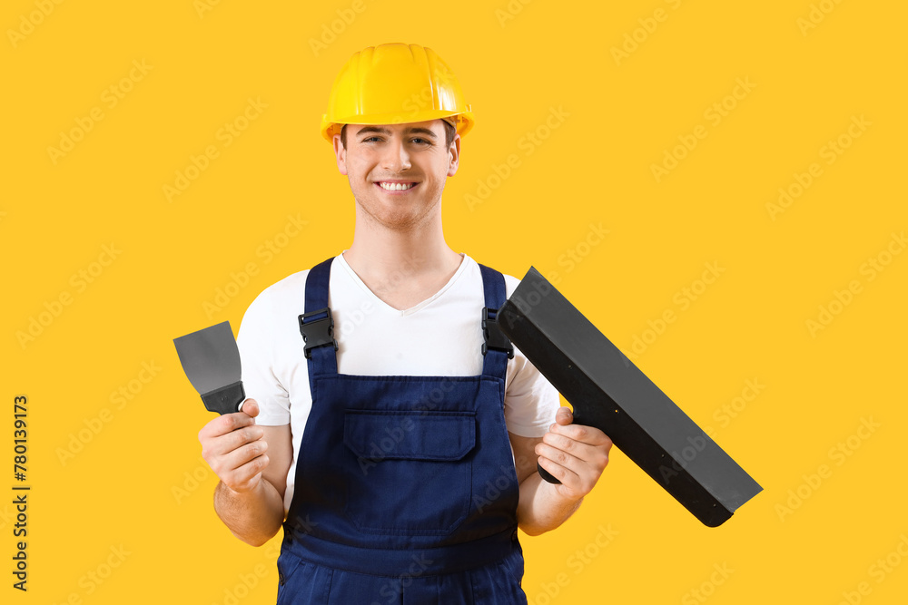 Male decorator with putty knives on yellow background