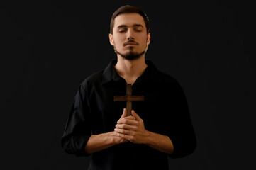 Sticker - Young man with wooden cross praying on black background