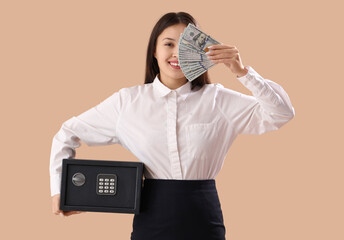 Sticker - Beautiful young happy Asian woman with safe box and money on brown background