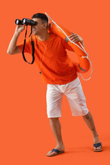 Canvas Print - Male lifeguard with ring buoy looking through binoculars on orange background