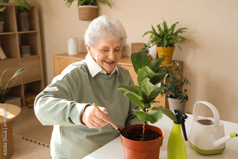 Senior gardener with shovel and plant on table at home