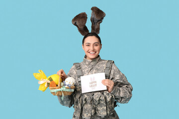 Sticker - Happy female soldier in bunny ears with greeting card, Easter basket and chocolate egg on blue background