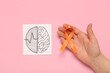 Drawing of brains and female hand with orange ribbon on pink background. Multiple Sclerosis Awareness Month