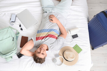 Canvas Print - Male tourist with travel accessories lying on bed in hotel room, top view