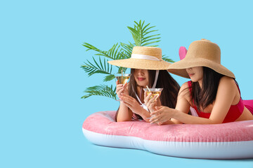 Sticker - Female Asian friends with cocktails lying on swim mattress against blue background