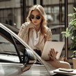 An attractive and beautiful business women with nice car ,phone and laptop with decent sun glasses and purse.