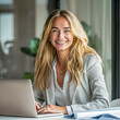 blonde smiling business woman sitting in front of laptop, with files at the desk