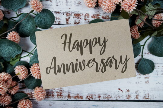 Happy Anniversary text message on paper card with flowers border frame on wooden background