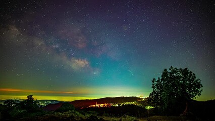 Poster - stars and milky way glide by in a blue sky above a green hilly landscape.