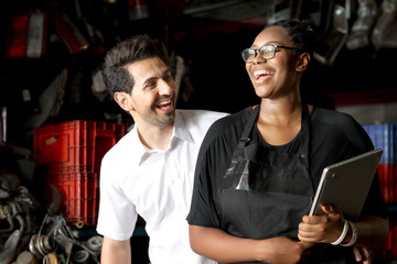 Wall Mural - Portrait of happy harmony people working together at workplace, smiling African American woman holds laptop with her colleague at auto spare parts store warehouse, surrounded by secondhand engine part