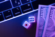Close-up view of modern laptop keyboard with dices and dollar bills fragments scattered on the keys, symbolizing the concept of online casino and dice games on a digital platform.
