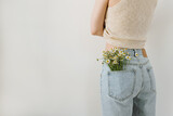 Fototapeta Tulipany - Young pretty woman with chamomile flowers bouquet in jeans pocket. Backside view