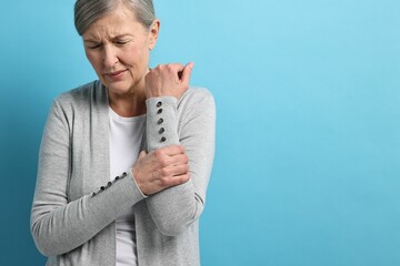 Wall Mural - Arthritis symptoms. Woman suffering from pain in arm on light blue background