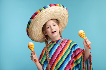 Wall Mural - Cute girl in Mexican sombrero hat and poncho dancing with maracas on light blue background
