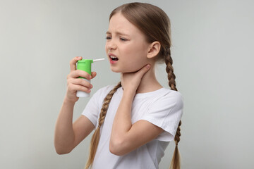 Canvas Print - Little girl using throat spray on light grey background