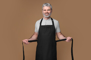 Poster - Happy man wearing kitchen apron on brown background. Mockup for design