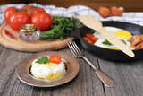 Fototapeta Koty - On a wooden table is a plate with fried egg, tomato and greens.