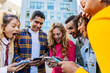 © Xavier Lorenzo - Group of young people using mobile phone together at city street. Millennial student friends enjoying social media content or playing video games on cellphone app at college campus