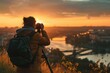 Back view of the photographer with backpack taking urban landscape with camera on tripod from hill. City, river, bridge during beautiful sunset. Hobby, active lifestyle, travel, people concept