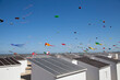 © yaqui_villegas - A clear sky dotted with colorful kites flying high above quaint beach huts on a sunny day