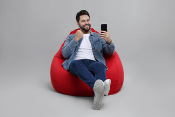 Wall Mural - Happy young man using smartphone on bean bag chair against grey background