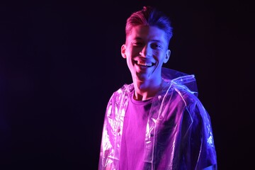 Poster - Young man wearing clear coat on dark background in neon lights. Space for text