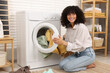 Woman putting laundry into washing machine indoors