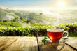 cup of hot tea on wooden table with sunny tea plantation on the background