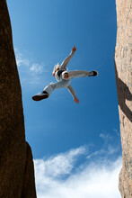 Directly Below View Of Young Woman Jumping Over Rock Formations Against Sky On Sunny Day