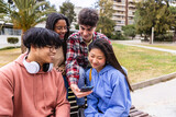 Fototapeta Londyn - Happy student friends using mobile phone together sitting at college campus. Education and technology concept.