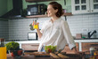 Young caucasian smiling woman drinking orange juice while standing in the kitchen at home, vitamins and healthy eating